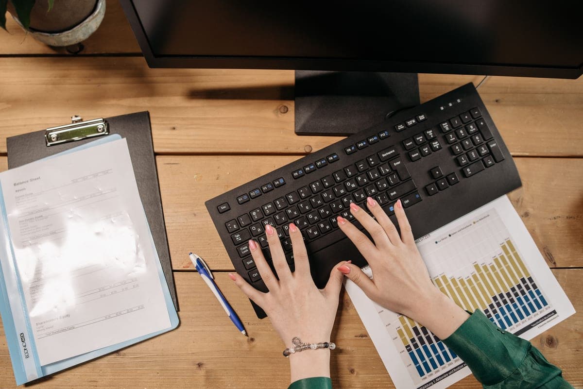 Office desk with a monitor displaying a spend report and a notebook of figures